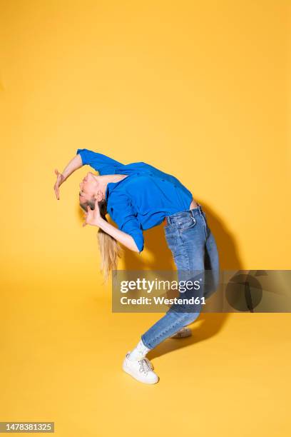 woman bending over backwards against yellow background - older woman bending over stock pictures, royalty-free photos & images