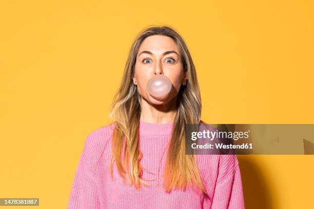 woman blowing bubble gum against yellow background - bubble gum stock pictures, royalty-free photos & images