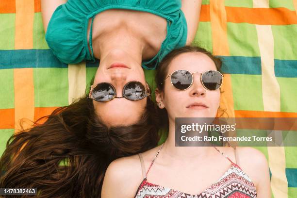 gorgeous three young girls wearing sunglasses lying on their backs on the floor looking at the camera - sunglasses overhead fotografías e imágenes de stock