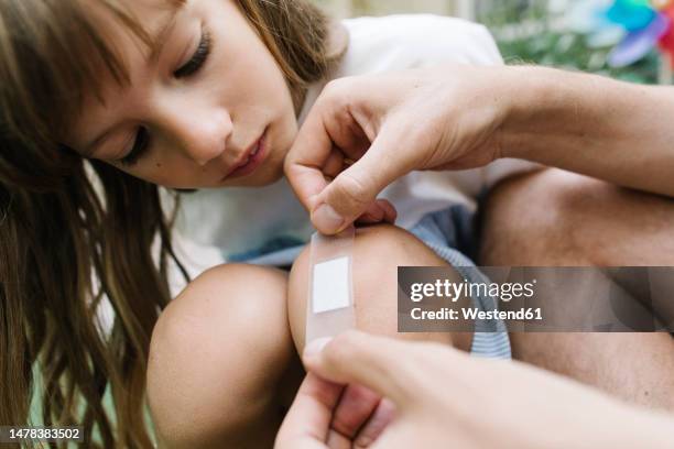father applying bandage on daughters knee - knees together - fotografias e filmes do acervo