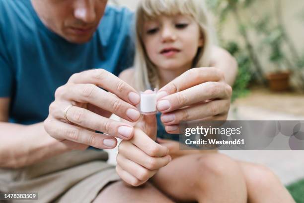 father applying bandage on daughters thumb - wundversorgung stock-fotos und bilder