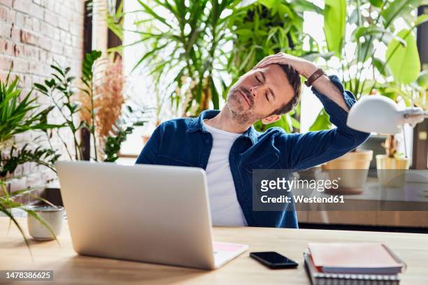 businessman stretching neck after work at loft office - desk stock pictures, royalty-free photos & images
