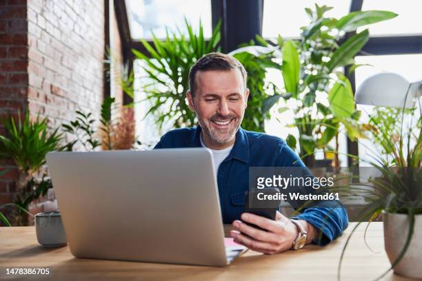 happy businessman with laptop using smart phone at loft office - geschäftsmann im büro mobiltelefon stock-fotos und bilder
