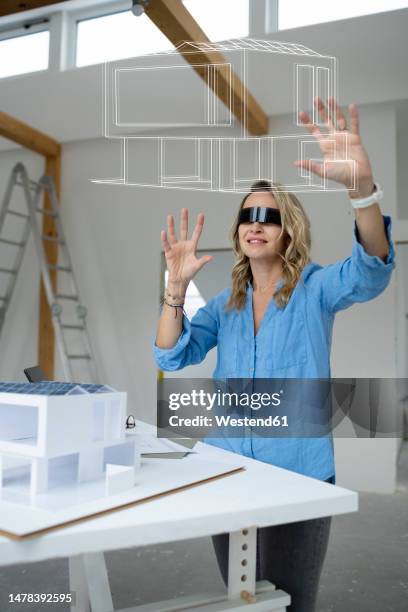 smiling architect wearing virtual reality simulator examining house model over table - demolition site stock illustrations