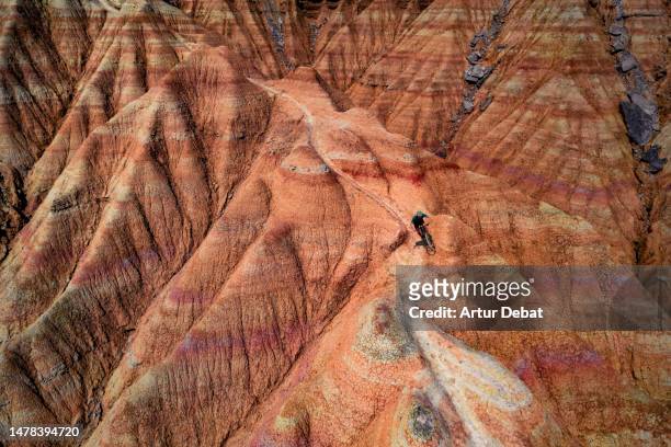 majestic aerial view of a mountain biker descending the desert badlands of the bardenas reales in spain with sinuous trail between sandstone formations. - extreme sports bike stock pictures, royalty-free photos & images