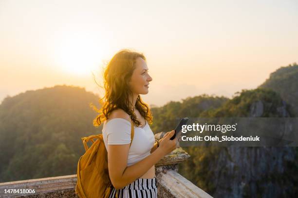 woman using smartphone on the top of wat tham sua in krabi at sunset - woman smartphone nature stockfoto's en -beelden