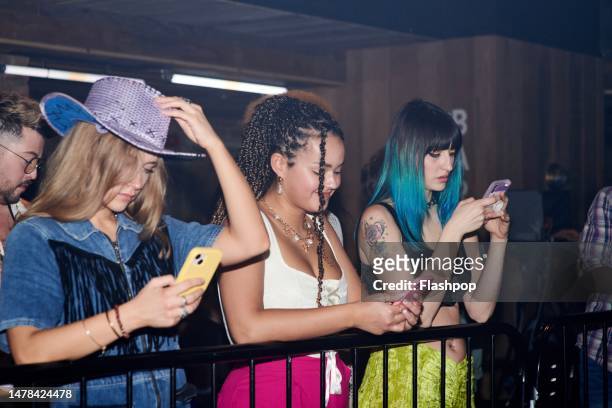 three women looking at their phones at a music event. - hand mobile stock-fotos und bilder