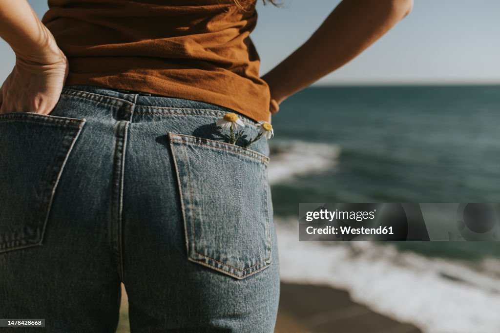 Flowers in back pocket of jeans worn by woman at beach