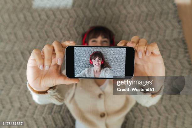 woman taking selfie through smart phone lying on floor at home - lying on back photos stock pictures, royalty-free photos & images