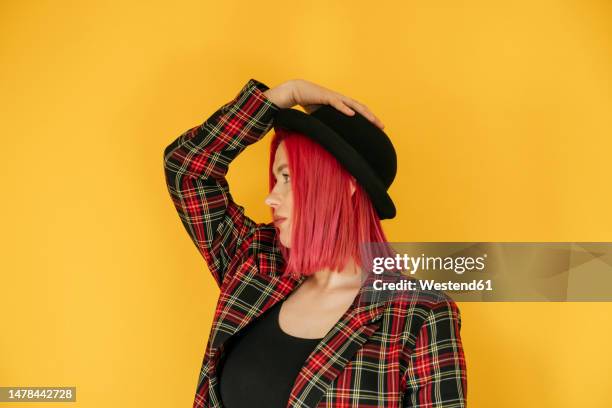 thoughtful woman wearing bowler hat standing against yellow background - melone hut stock-fotos und bilder