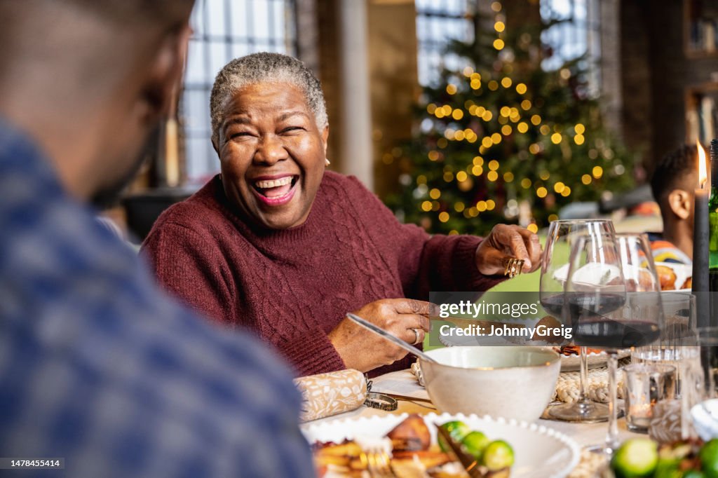 Senior black woman laughing at dinner table on Christmas Day
