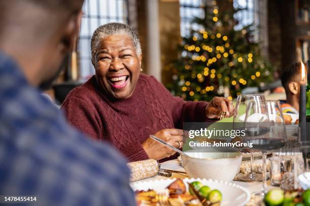 senior black woman laughing at dinner table on christmas day - cuisine humour stock pictures, royalty-free photos & images