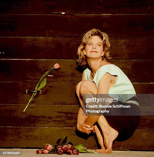 Actor Meg Ryan poses in front of wooden fence with roses, hugging her knees, in Los Angeles in 1987.