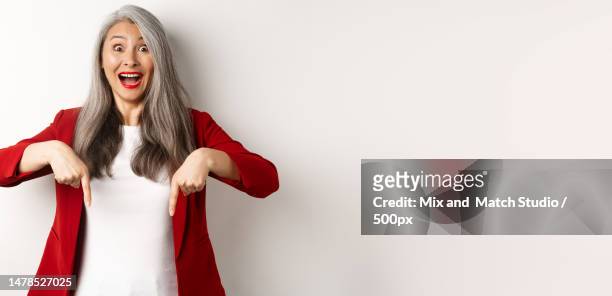 portrait of happy asian lady in red blazer showing logo,pointing - down feather stock pictures, royalty-free photos & images