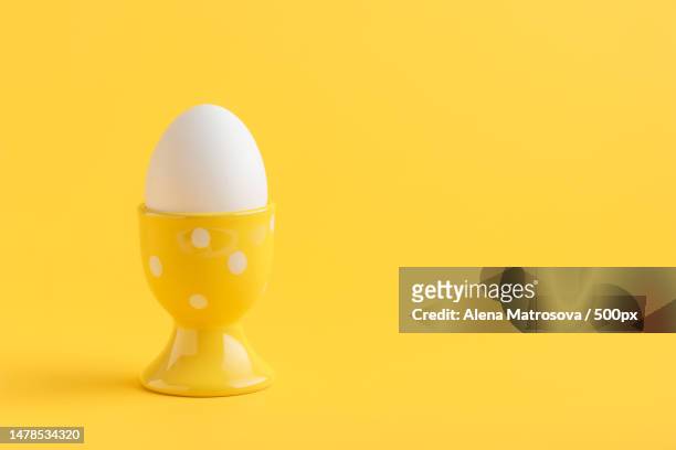 white egg in a yellow egg holder standing on yellow background,helsinki,uusimaa,finland - eierbecher stock-fotos und bilder