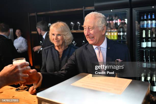 Camilla, Queen Consort looks on as King Charles III pours a beer at a reception at Schuppen 52 on March 31, 2023 in Hamburg, Germany. The King and...