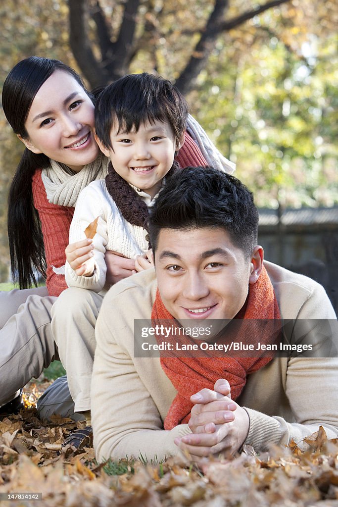 Young family lying on the grass surrounded by Autumn leaves