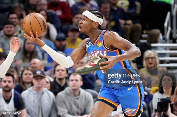 Shai Gilgeous-Alexander of the Oklahoma City Thunder reaches for a rebound while holding his shoe against Indiana Pacers at Gainbridge Fieldhouse on...