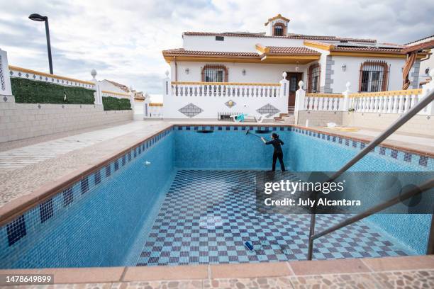 woman scrubs the empty pool with a broom after emptying. preparing for summer - swimming pool cleaning stock pictures, royalty-free photos & images