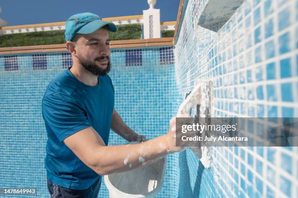 bearded man spreads the cement grout on the pool tile to waterproof it, preparing pool for summer - swimming pool maintenance stock pictures, royalty-free photos & images