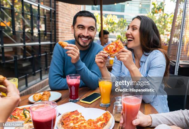 happy couple eating pizza with a group of friends - restaurant stockfoto's en -beelden