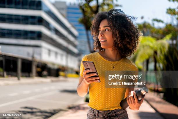 young woman walking on the street using her cell phone - colombia street stock pictures, royalty-free photos & images