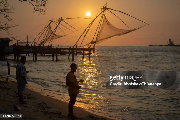 Fisherman casts a line to catch fish in front of Chinese fishing nets on Fort Kochi Beach on April 01, 2023 in Kochi, India.