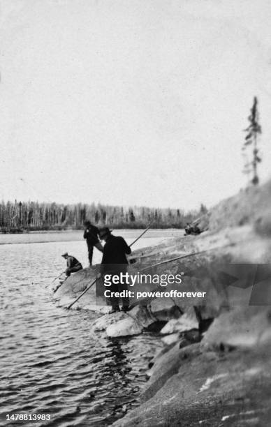 men fishing with rods and spear at wekusko lake in manitoba, canada  - 1924 - man spear fishing stock pictures, royalty-free photos & images