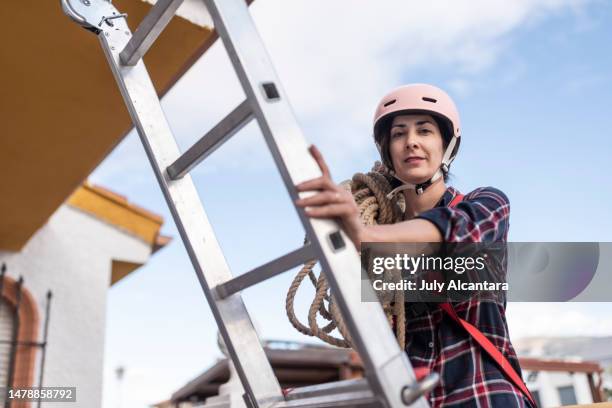 donna esperta in lavori verticali con casco e imbracatura, occupandosi dell'installazione e manutenzione di pannelli solari - attrezzatura di sicurezza foto e immagini stock
