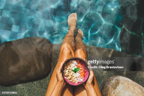 woman's hand holding fresh fruit smoothie bowl on background of turquoise water in swimming pool - bali stock pictures, royalty-free photos & images