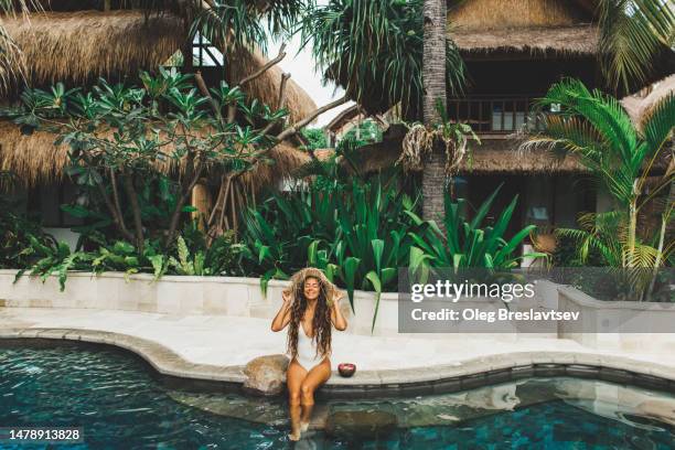 young happy woman relaxing on poolside. travel and vacations in asia. straw hat and white swimsuit. - bali luxury bildbanksfoton och bilder