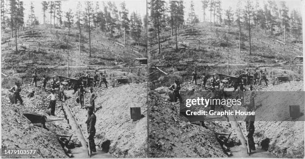 Stereoscopic image showing gold prospectors standing on either side of a rocker box, a device used for separating alluvial placer gold, as they mine...