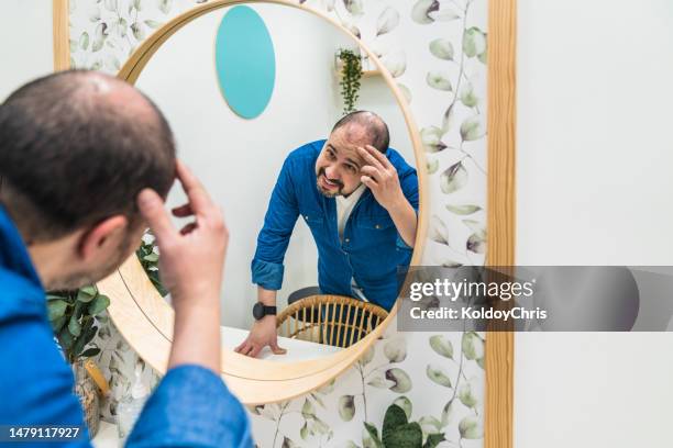 male person looking at himself in front of a mirror with a worried face - balding stock pictures, royalty-free photos & images