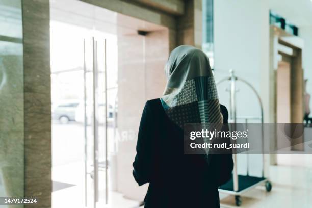une femme d’affaires musulmane poussant la porte de l’hôtel pour quitter le hall de l’hôtel avec sa valise. - voile religieux photos et images de collection