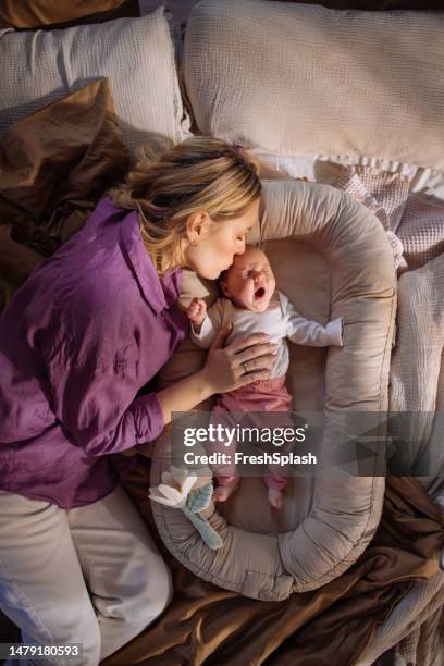 a happy beautiful blonde woman taking care of her adorable newborn child - yawning mother child stock pictures, royalty-free photos & images