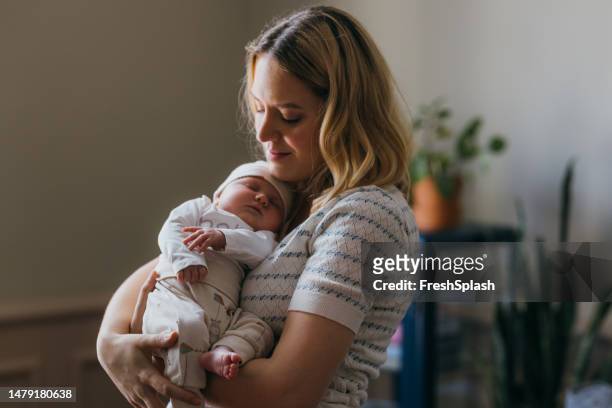 a happy beautiful blonde woman with her eyes closed taking care of her adorable newborn child who is sleeping in her arms - beautiful blonde babes 個照片及圖片檔