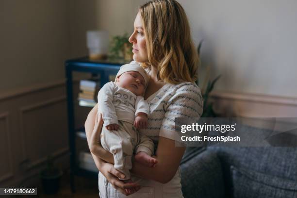 a serious beautiful blonde woman looking away while taking care of her adorable newborn child - beautiful blonde babes stock pictures, royalty-free photos & images