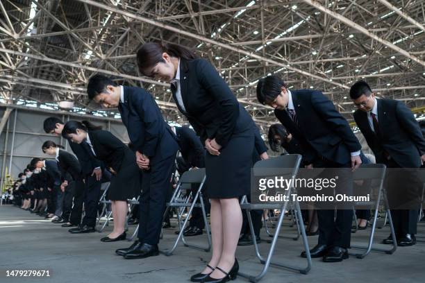 Newly hired employees for Japan Airlines bow during an entrance ceremony in a hangar at Haneda Airport on April 03, 2023 in Tokyo, Japan. 2,000 new...