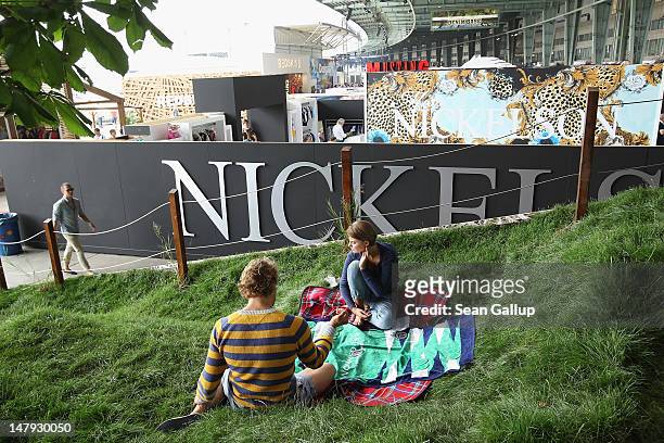 Models playing backgammon recline on real grass as visitors walk past at the Hilfiger Denim stand at the 2012 Bread & Butter fashion trade fair at...