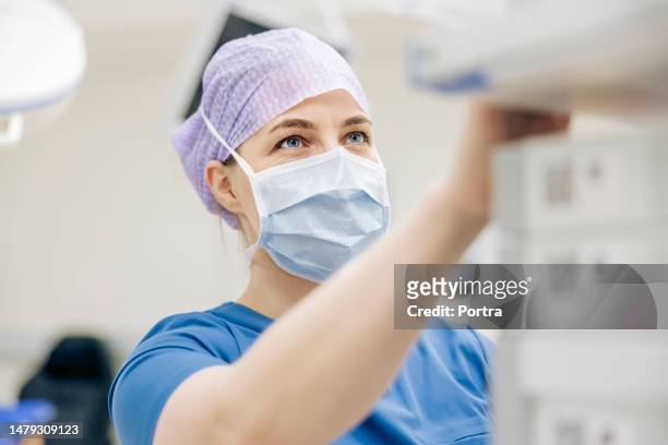 female medical surgeon controlling medical equipment during surgery - hospital safety stock pictures, royalty-free photos & images