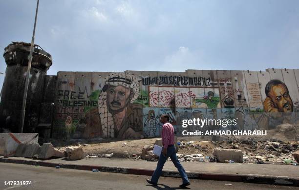 Palestinian man walks past a mural of late Palestinian leader Yasser Arafat and jailed Fatah leader Marwan Barghuti on a section of Israel's...