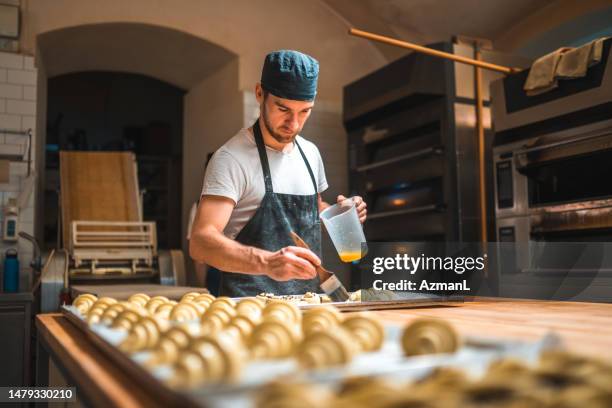 handwerklicher bäcker, der in einer kleinen bäckerei eier auf gebäck aufträgt - arbeitsplatte stock-fotos und bilder