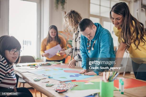 personas con síndrome de down y parálisis cerebral haciendo un proyecto de arte con ayuda de asistentes y animadores. taller de arte para el cuidado de la salud de la discapacidad. - discapacidad del desarrollo fotografías e imágenes de stock