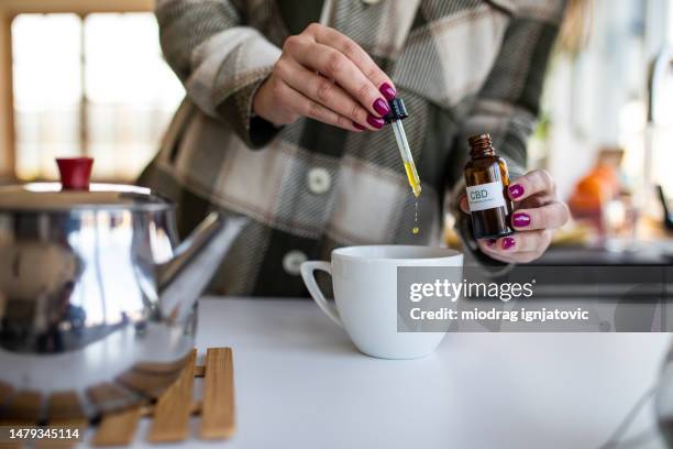 mujer añadiendo aceite de cbd en el té - cannabinoid fotografías e imágenes de stock