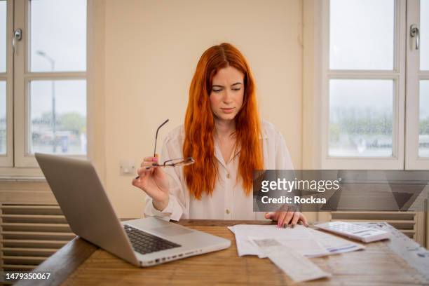 young woman using calculator while going through bills and home finances - student loan stockfoto's en -beelden