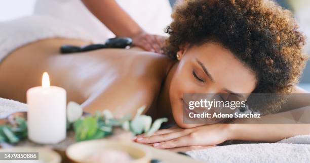 relax, spa and zen woman for hot stone and physical therapy in room. female client on table with candles and smile for luxury cosmetics treatment for back, health and wellness of body and mind - tranquility spa stock pictures, royalty-free photos & images