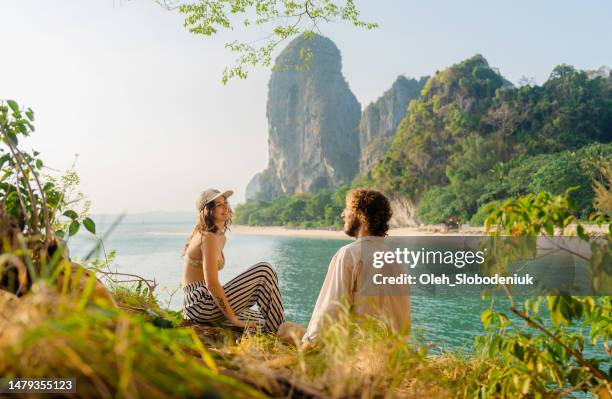 mulher e homem sentados no penhasco no fundo da baía de railey - phuket - fotografias e filmes do acervo