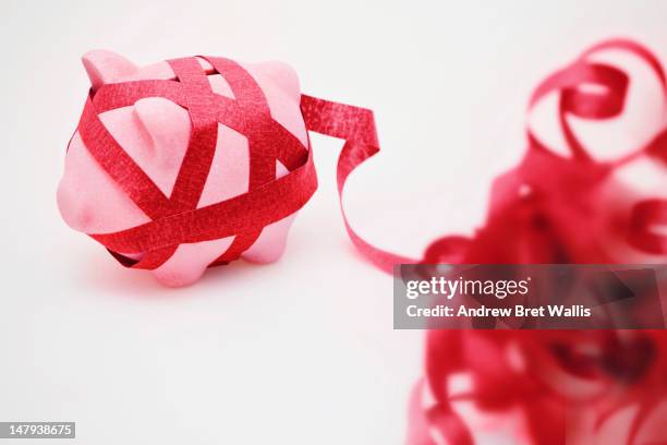 piggy bank wrapped in a ball of red tape - red tape expressão inglesa imagens e fotografias de stock