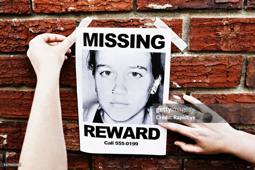 Female hands attach &quot;Missing&quot; poster of teenage girl to wall
