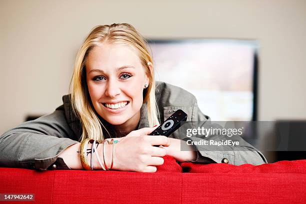 smiling blonde with remote control looks over back of couch - lcd tv stock pictures, royalty-free photos & images